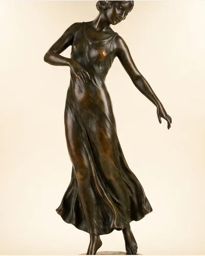 A patinated bronze figure of a dancer on a marble socle, photographed on a warm paper plate.
