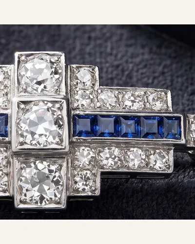 An Art Deco platinum brooch set with old-cut diamonds and calibré-cut sapphires, on charcoal velvet. — the calibré border.