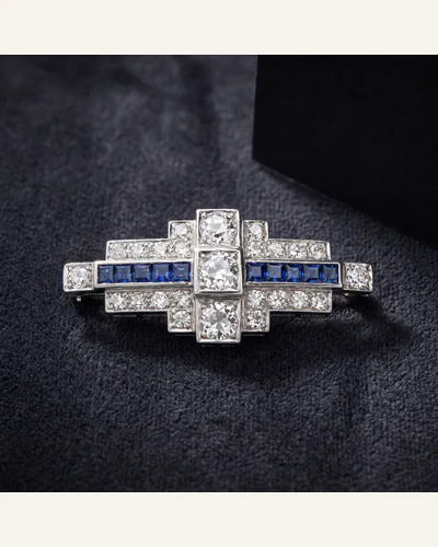 An Art Deco platinum brooch set with old-cut diamonds and calibré-cut sapphires, on charcoal velvet.