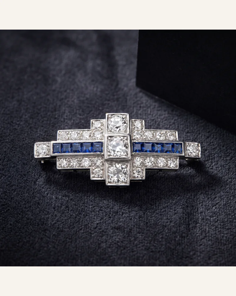 An Art Deco platinum brooch set with diamonds and sapphires on charcoal velvet.