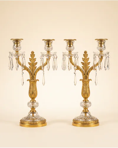 A pair of Regency ormolu and cut-glass candelabra hung with lustre drops, photographed on a warm paper plate.