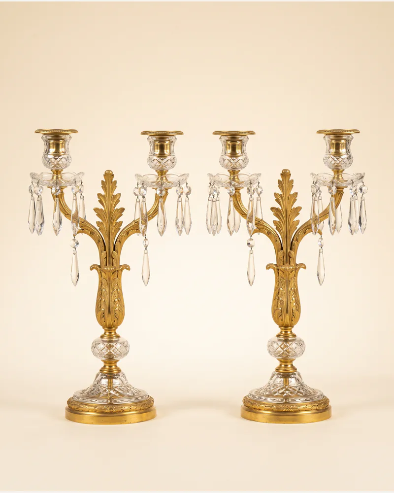 A pair of Regency ormolu and cut-glass candelabra hung with lustre drops, photographed on a warm paper plate.