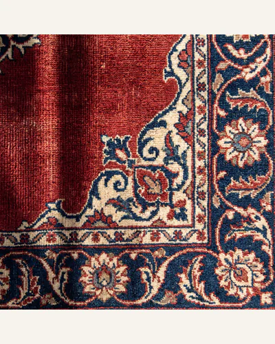 The corner of an antique hand-knotted Persian carpet with a madder-red field and palmette border.