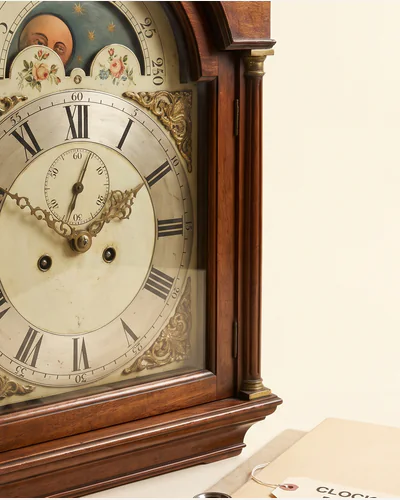 An ebonised bracket clock with brass mounts and a painted dial, photographed on a warm paper plate.