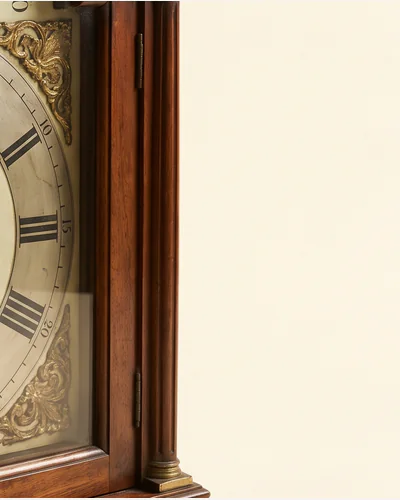 An ebonised bracket clock with brass mounts and a painted dial, photographed on a warm paper plate. — the mounts.