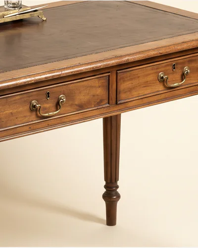 An antique walnut writing desk with a leather inset top and turned legs, photographed on a warm paper plate. — the splice.