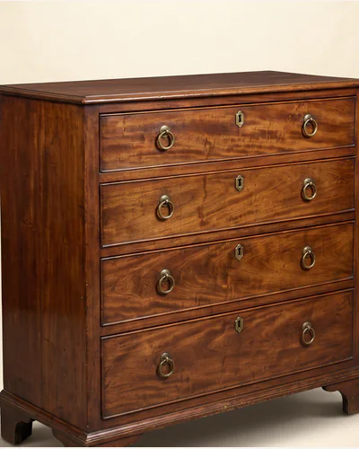 A mahogany serpentine chest of drawers with brass handles, three-quarter view on a paper plate.