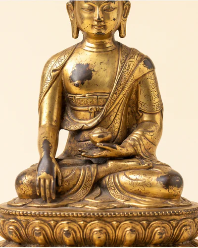 A gilt bronze figure of a seated bodhisattva on a double-lotus base, photographed on a warm paper plate. — the robes.