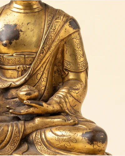 A gilt bronze figure of a seated bodhisattva on a double-lotus base, photographed on a warm paper plate. — the gilding.