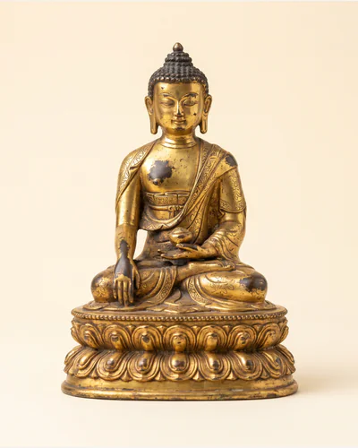 A gilt bronze figure of a seated bodhisattva on a double-lotus base, photographed on a warm paper plate.