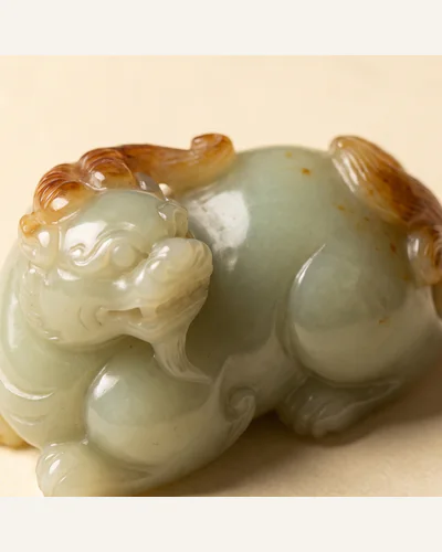 A pale celadon jade carving of a recumbent beast with russet inclusions, photographed under macro lighting. — the carving.