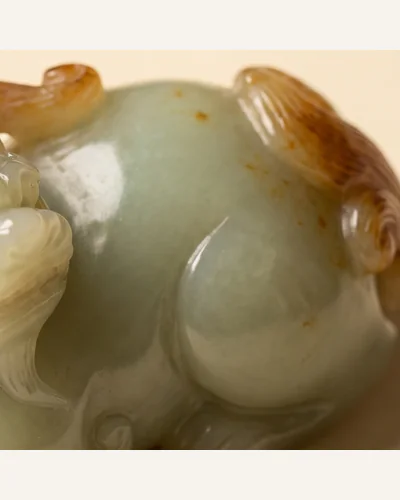 A pale celadon jade carving of a recumbent beast with russet inclusions, photographed under macro lighting. — the russet inclusion.
