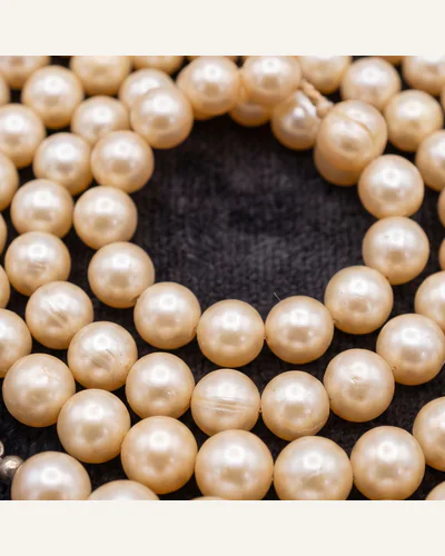A graduated strand of natural pearls with an antique diamond-set clasp, coiled on charcoal velvet. — the clasp.