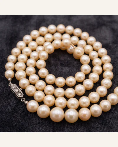 A graduated strand of natural pearls with an antique diamond-set clasp, coiled on charcoal velvet.