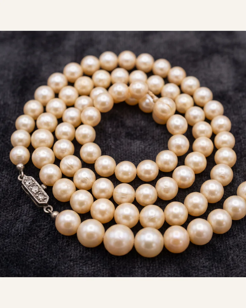 A graduated strand of natural pearls with an antique diamond-set clasp, coiled on charcoal velvet.