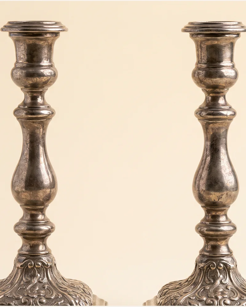 A pair of cast silver candlesticks with knopped stems and shaped square bases, on a warm paper plate.