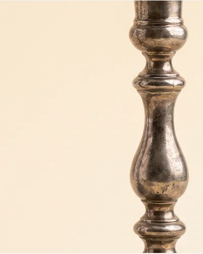 A pair of cast silver candlesticks with knopped stems and shaped square bases, on a warm paper plate. — the base.
