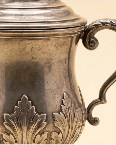 A silver two-handled cup and cover of baluster form with applied cut-card decoration. — the handles.