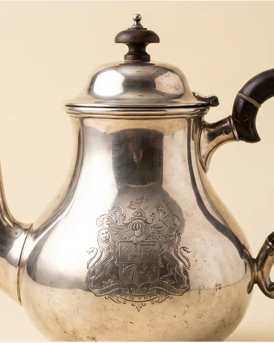 A Georgian sterling silver teapot with a fruitwood handle and an engraved crest. — the crest.