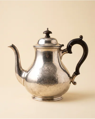 A Georgian sterling silver teapot with a fruitwood handle and an engraved crest.