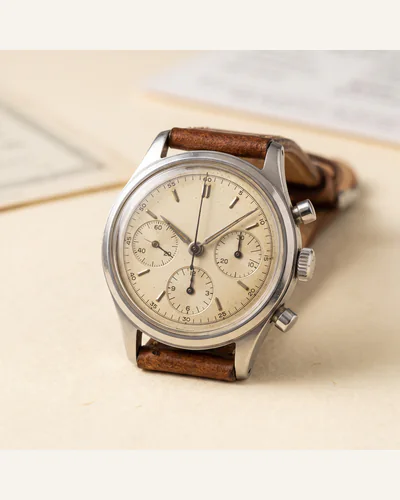 A vintage stainless steel chronograph wristwatch on a worn leather strap, photographed on a paper plate.